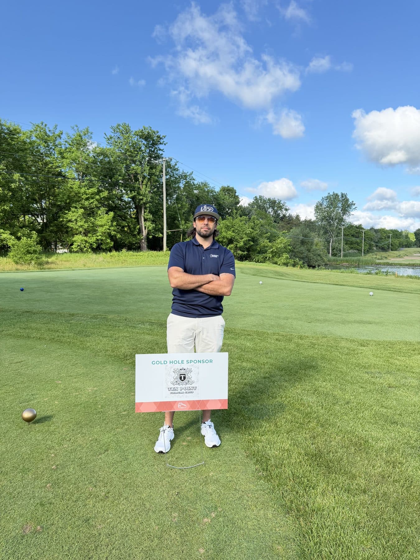 Anthony Buck beside the Ten Point Financial Group Gold Hole Sponsor sign at a charity golf outing